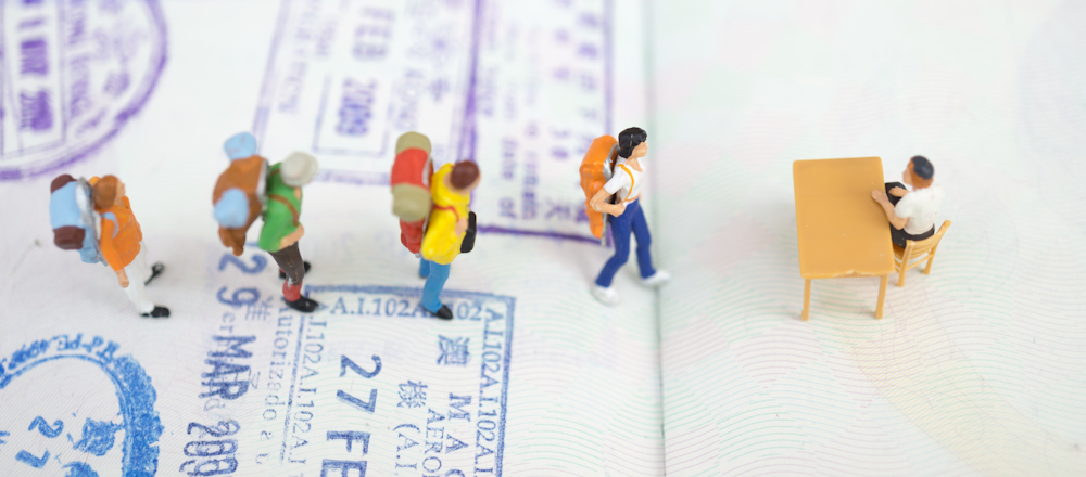 miniature tourist figurines queuing at customs on a passport page
